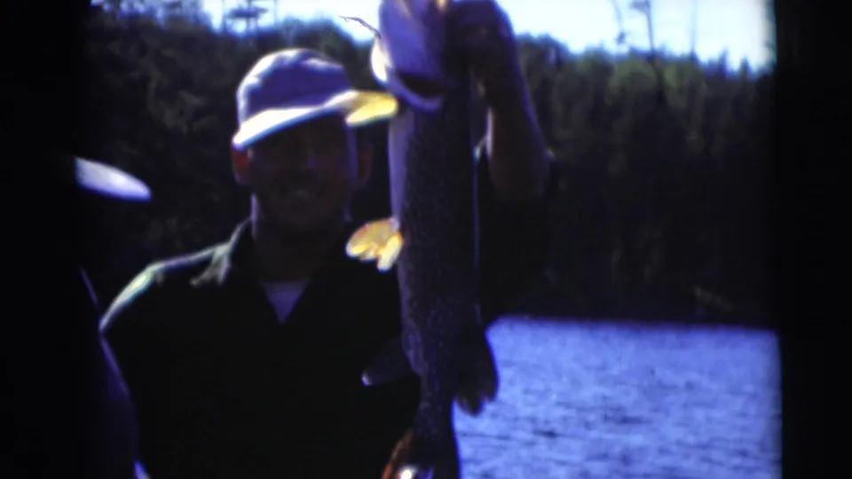 In supplied 1953 Baraboo, Wisconsin footage, a man in a cap holds up a large fish near blue lake water and trees.
