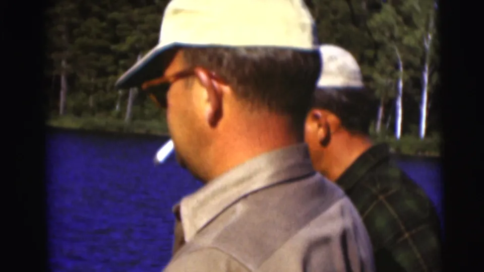 Two adult men in caps stand near a Wisconsin lake shore, one with a cigarette, in 1953 home-movie footage.