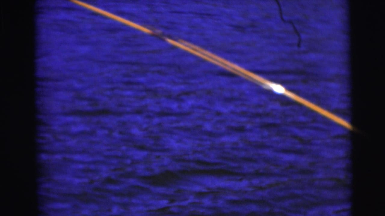 Bent fishing rod extending over dark blue water, with the angler mostly out of frame.