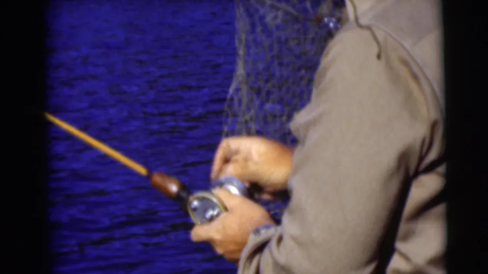 1953 Baraboo, Wisconsin 8mm frame showing the angler's hands on the reel and a landing net near the boat.