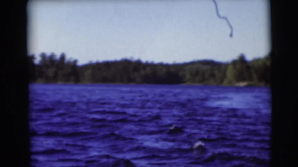 1953 home-movie lake view in Baraboo, Wisconsin, showing blue water, treeline, and low hills from a boat perspective.