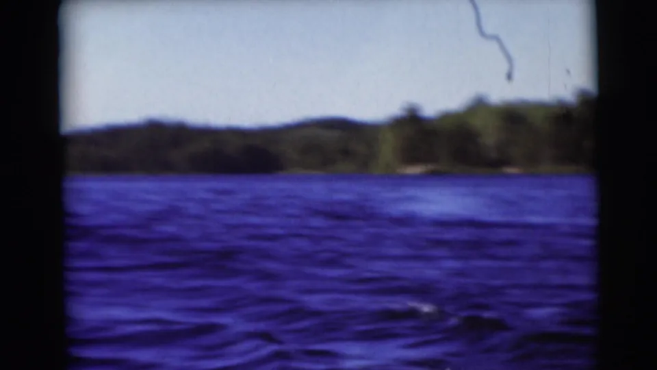 Wide 8mm frame of a Wisconsin lake near Baraboo, with rippled water, trees, and low hills under a bright sky.