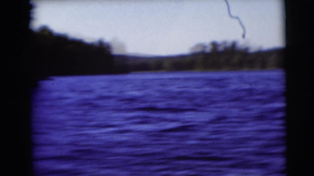 Soft 8mm view across rippled lake water toward a wooded shoreline and low hills.