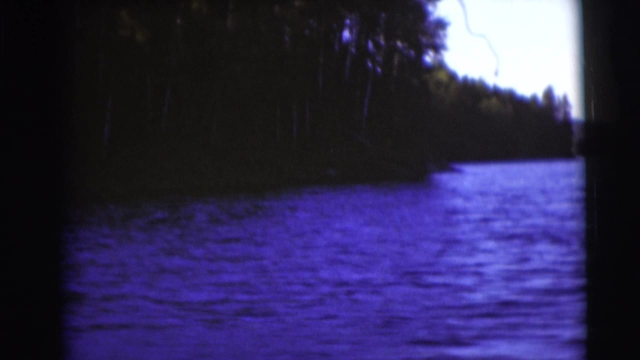 1953 Baraboo-area lake view on 8mm film, with dark trees along the shore and blue-purple water in the foreground.