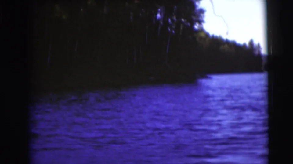 1953 Baraboo-area lake view on 8mm film, with dark trees along the shore and blue-purple water in the foreground.
