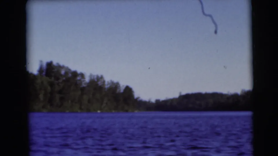 1953 Baraboo, Wisconsin lake scene on 8mm film, with blue water, distant wooded hills, and a lightly marked film frame.