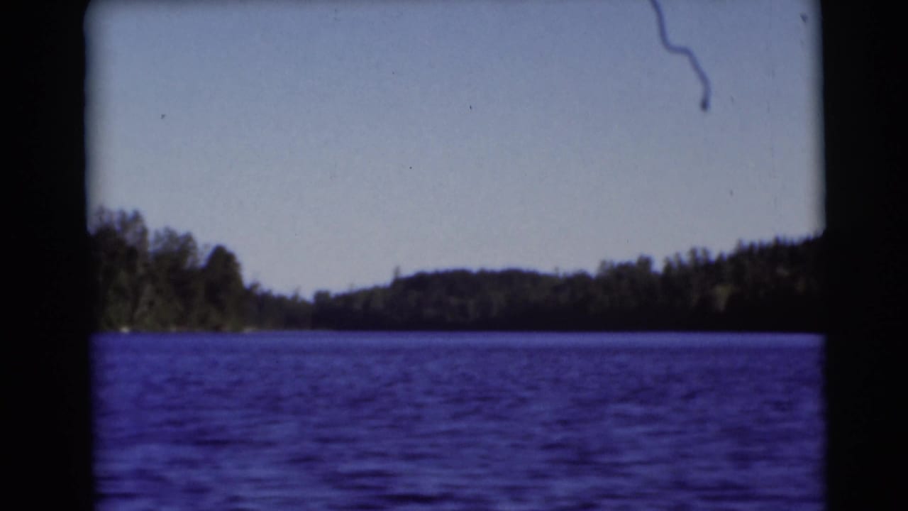 Blue lake water with wooded shoreline and pale sky framed by dark film edges.