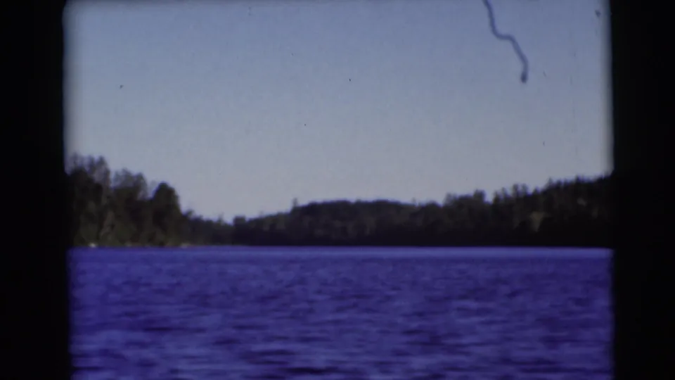 1953 Baraboo, Wisconsin 8mm frame showing blue lake water, distant trees, low hills, and dark film gate edges.