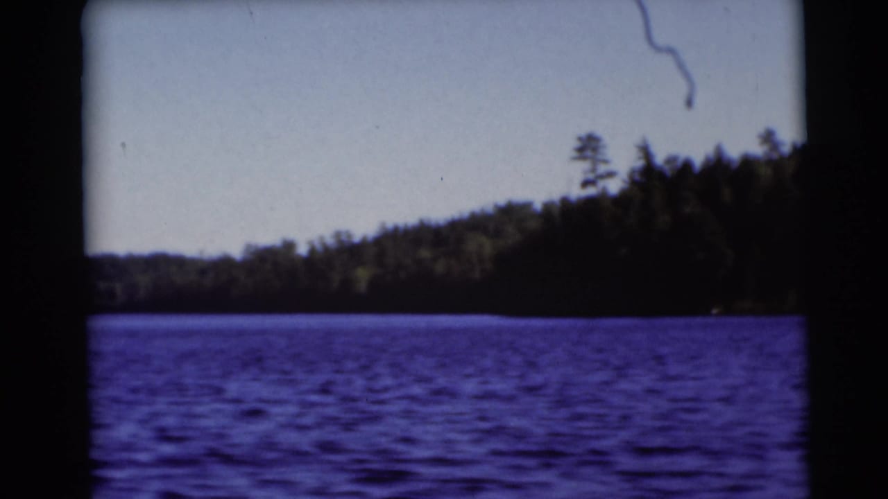 1953 Baraboo, Wisconsin lake scene with rippled blue water, dense trees along the shore, and visible 8mm frame edges.