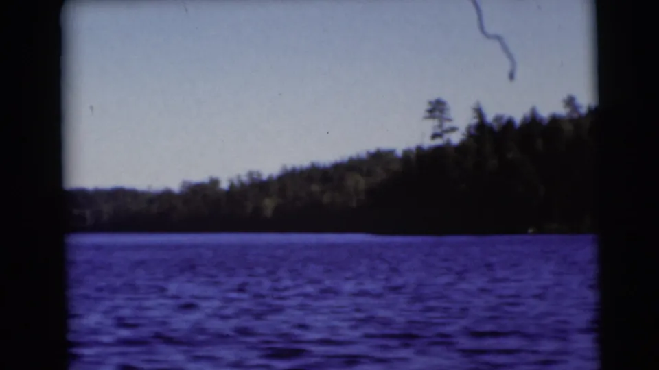 1953 Baraboo, Wisconsin lake scene with rippled blue water, dense trees along the shore, and visible 8mm frame edges.