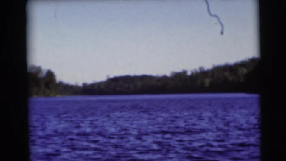 1953 Baraboo, Wisconsin 8mm view across blue lake water toward a wooded shoreline and low hills.