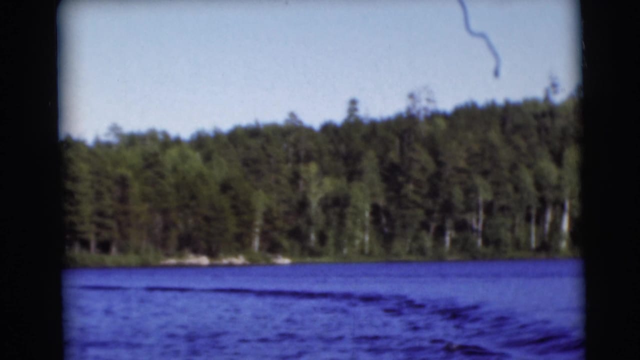1953 Baraboo-area 8mm frame showing a calm lake bordered by dense trees under daylight.