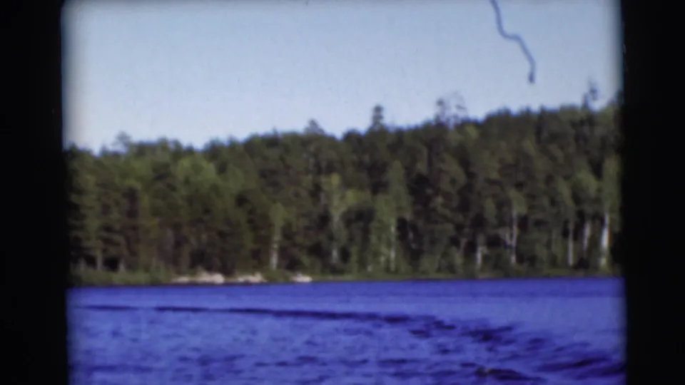 1953 Baraboo-area 8mm frame showing a calm lake bordered by dense trees under daylight.