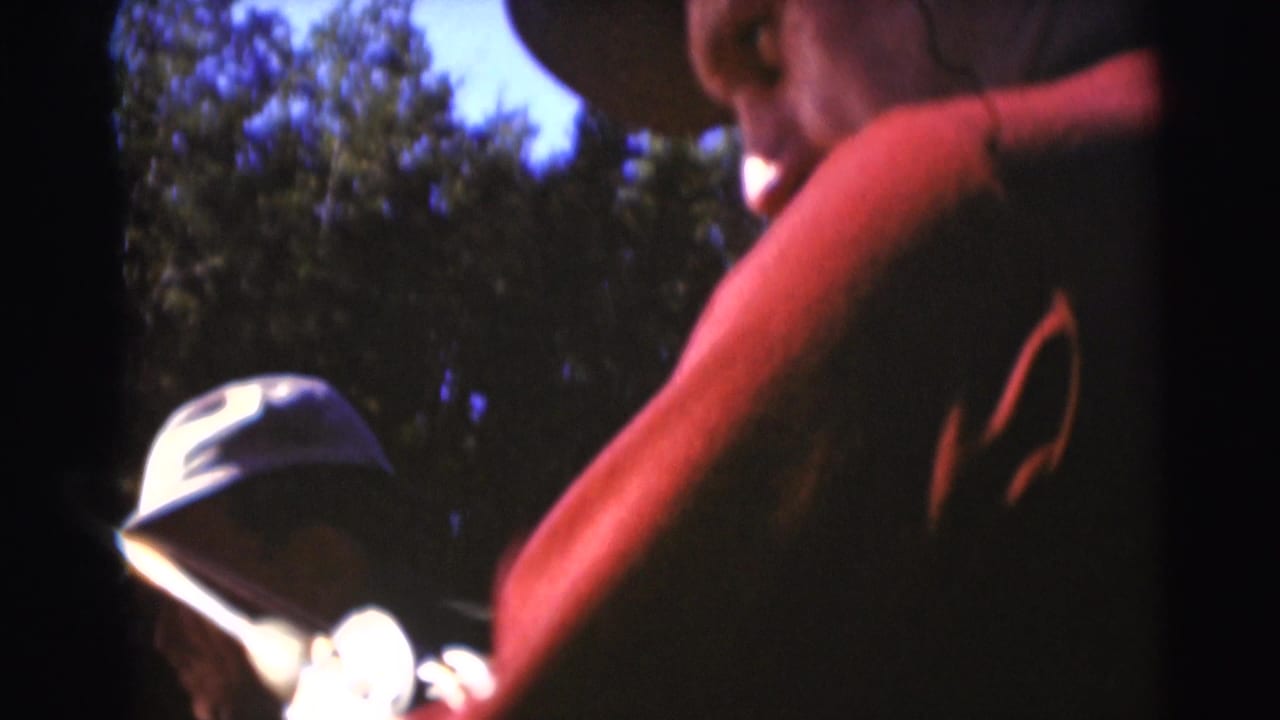 1953 Baraboo 8mm frame with a capped man and a red-shirted companion near trees on a fishing outing.
