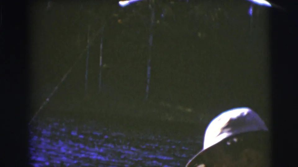 1953 Baraboo 8mm frame with a capped man partly visible beside dark water and wooded shoreline.