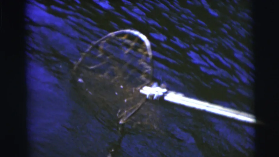 1953 Baraboo fishing frame showing a long-handled landing net held over rippled blue lake water.