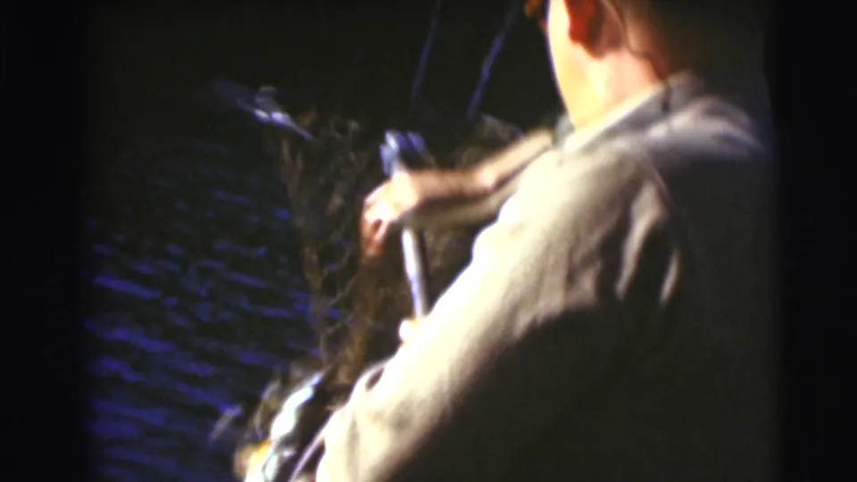 A man seen from behind handles a fishing net beside dark lake water in the 1953 Wisconsin footage.