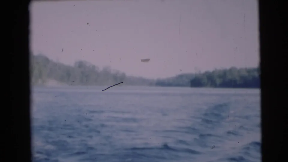 Boat wake trails across open water toward distant wooded banks in this 1953 Baraboo, Wisconsin 8mm home-movie frame.