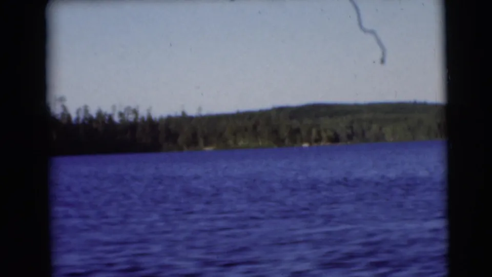 1953 8mm frame from a moving boat, with rippled lake water in front and dense trees along the far Baraboo-area shore.