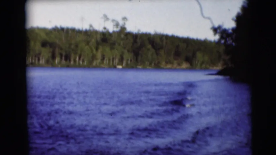 1953 Baraboo, Wisconsin lake scene from a boat, showing foamy wake, blue water, shoreline trees, and 8mm film edges.