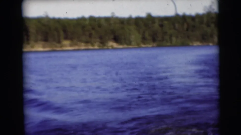 1953 Baraboo, Wisconsin lake view with blue water, a wooded shore, pale sky, and visible 8mm film edges.