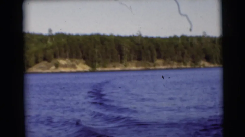 1953 Baraboo, Wisconsin 8mm frame showing wake patterns on lake water and a tree-lined shore beyond.
