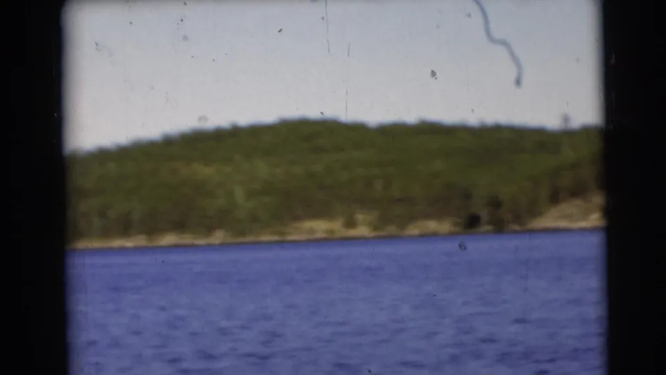 1953 Baraboo, Wisconsin lake scene with a low forested hill, calm blue water, and visible 8mm film wear.