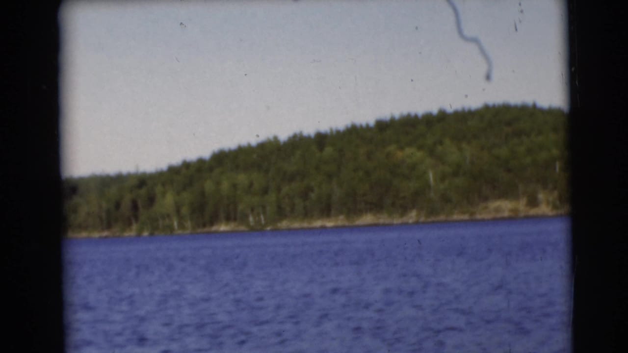 Tree-lined shoreline across blue lake water with film gate edges visible.