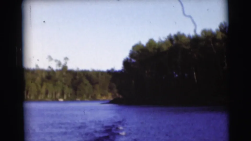 1953 Baraboo, Wisconsin home-movie frame looking across lake water toward a darker wooded shore.