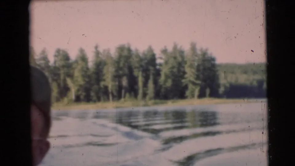 1953 Baraboo, Wisconsin 8mm frame showing river wake, distant trees, and a partial passenger profile at the left edge.
