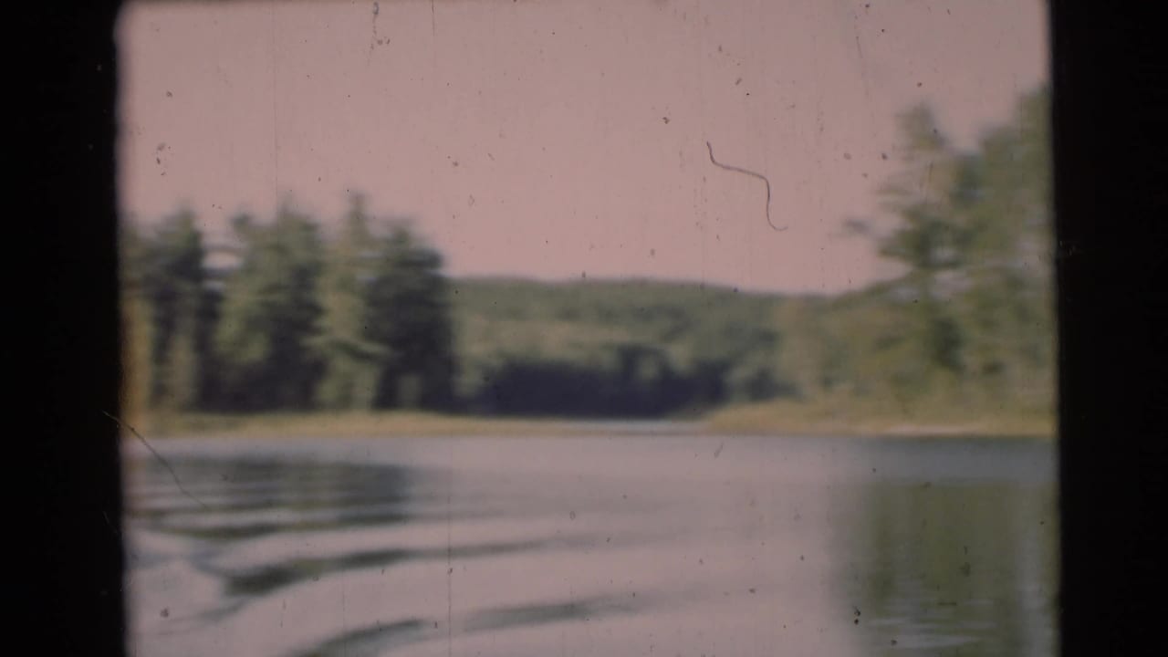 1953 Baraboo, Wisconsin home-movie frame looking from a moving boat across calm lake water toward trees and low hills.