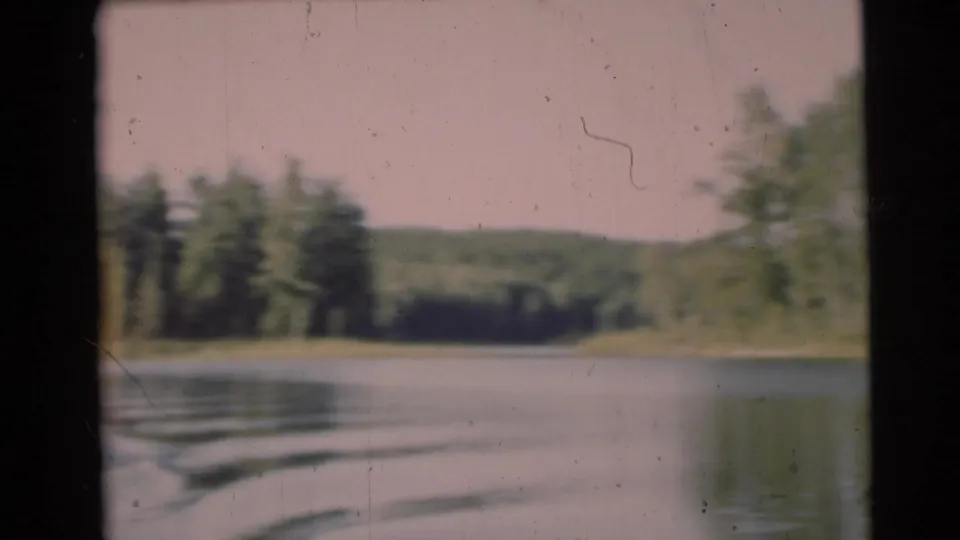 1953 Baraboo, Wisconsin home-movie frame looking from a moving boat across calm lake water toward trees and low hills.