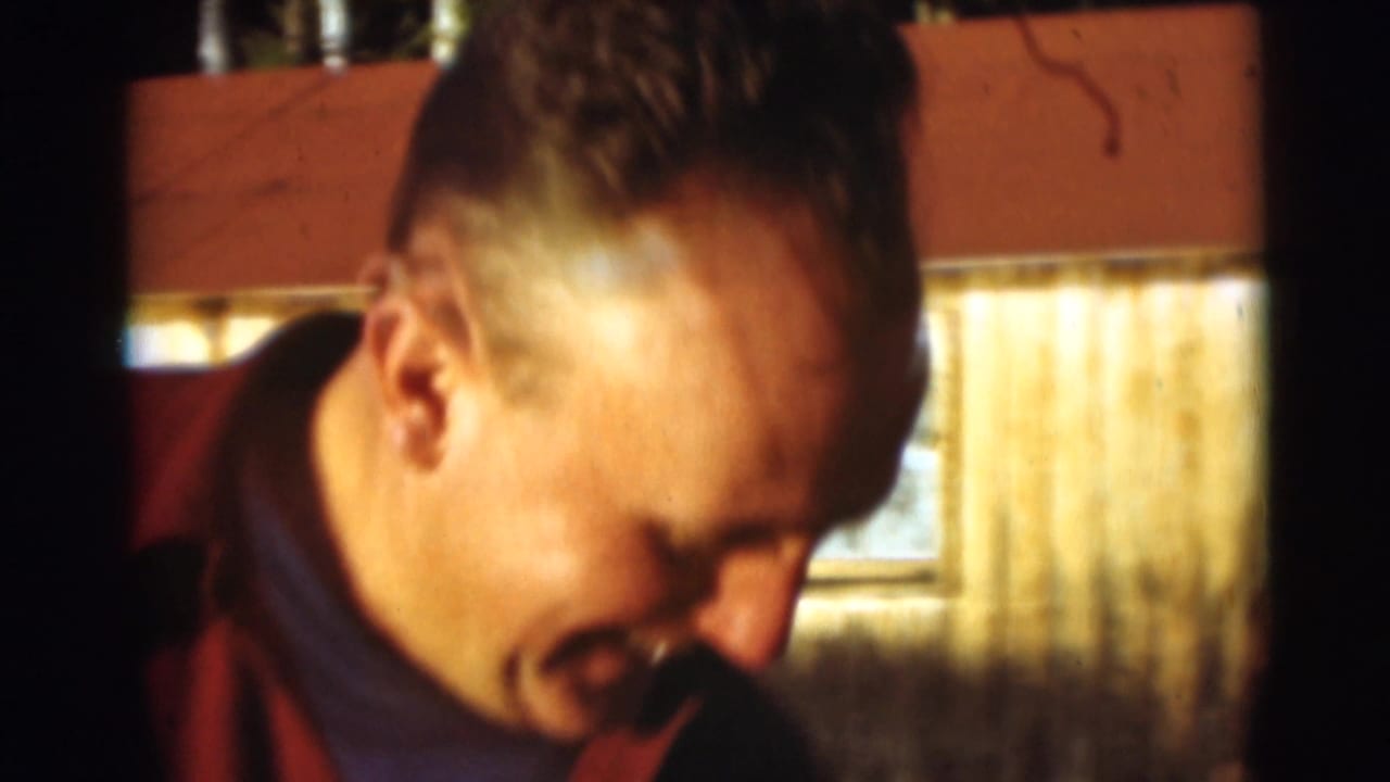 In 1953 Baraboo home-movie footage, an adult man in plaid outerwear smiles near a sunlit rustic exterior.