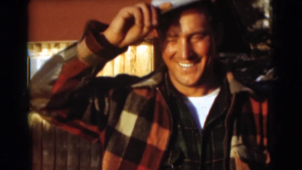 An adult man in a white cap and plaid outerwear smiles toward the camera in 1953 Baraboo home-movie footage.