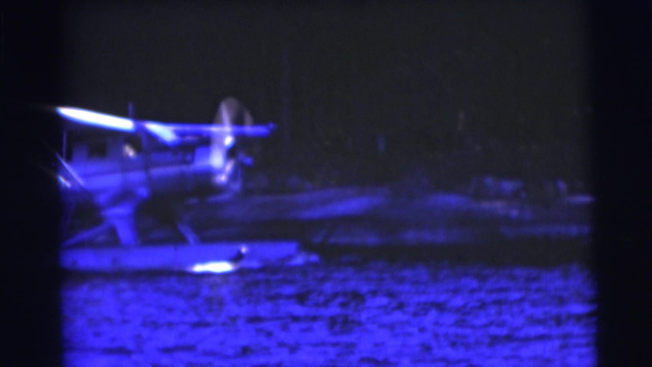 1953 Baraboo, Wisconsin 8mm frame showing a blue-tinted night view of a floatplane on a lake with propeller blur.