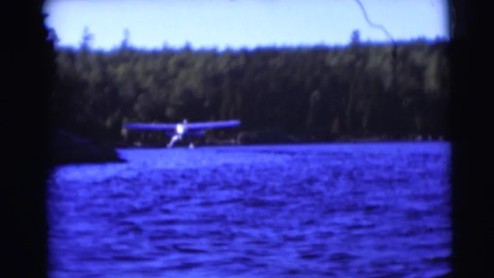 1953 Baraboo, Wisconsin home-movie frame showing a floatplane on lake water against a wooded shore.