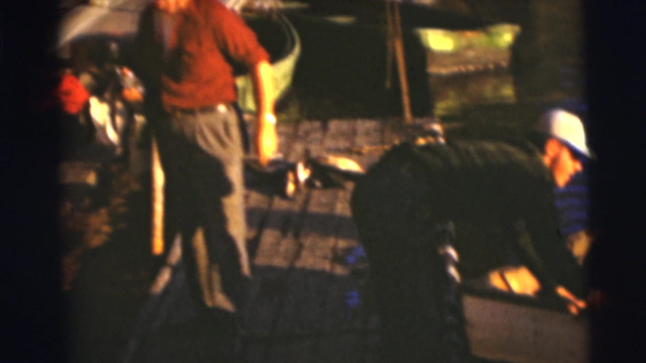 Two men on a wooden dock near small boats and fishing gear.