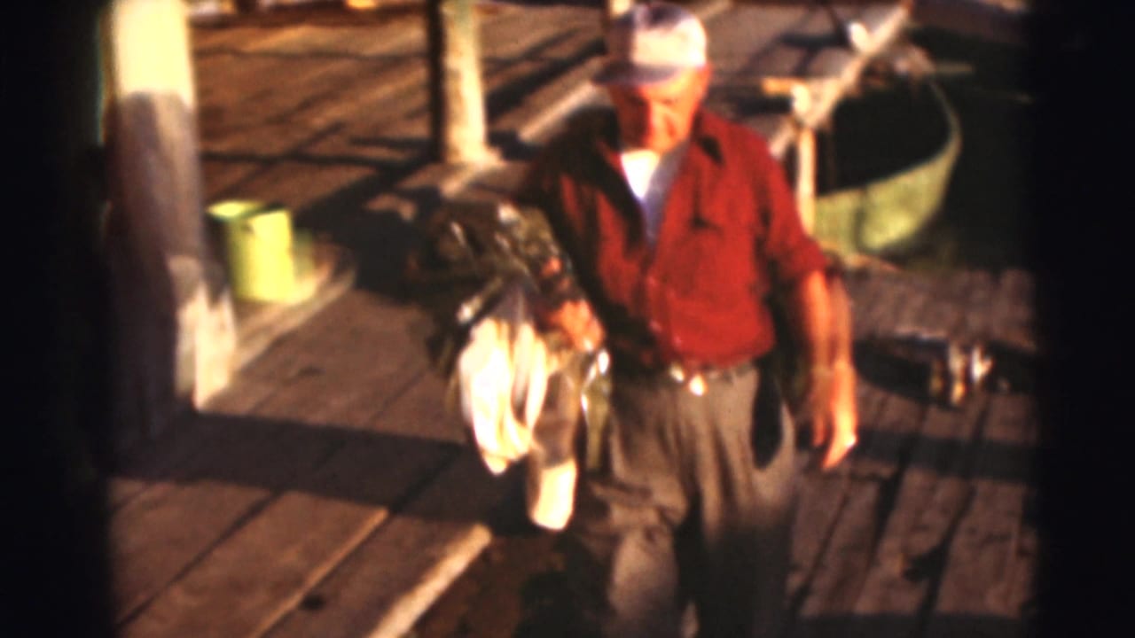 Man in a red shirt walks on a dock carrying gear and a white cloth.