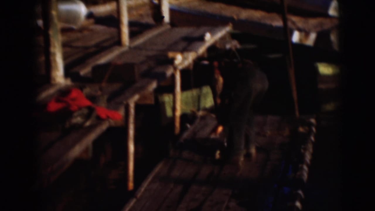 Man bends over on a wooden dock near fishing gear and water.