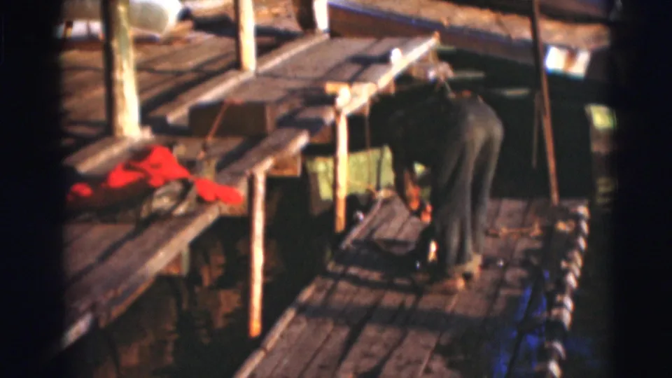 The fisherman continues working on the dock, with a red life vest and water visible beside the planks.