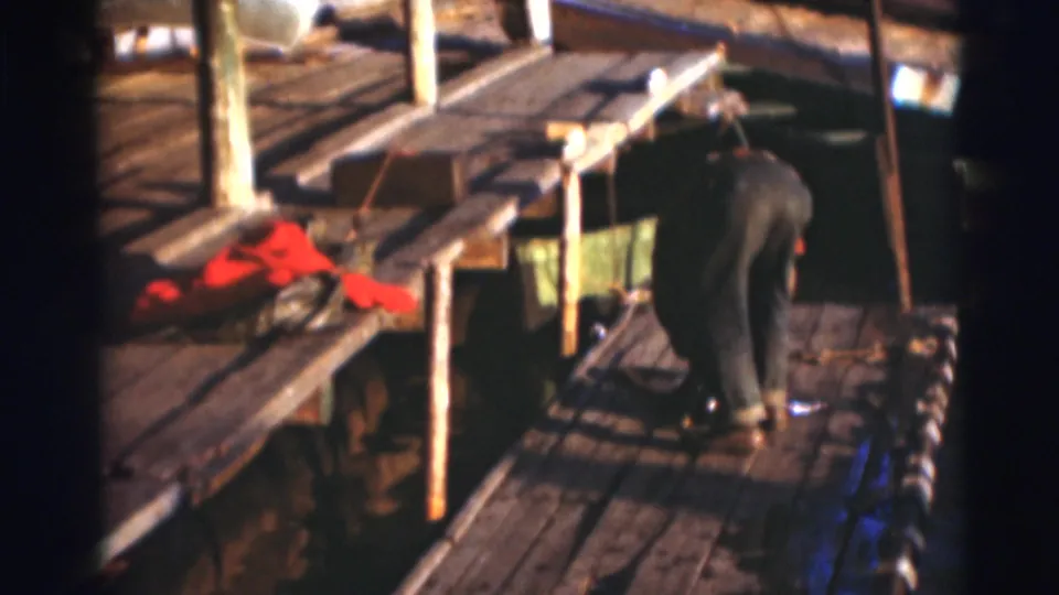 A fisherman bends near the edge of a wooden dock in the 1953 Baraboo, Wisconsin archival home-movie clip.
