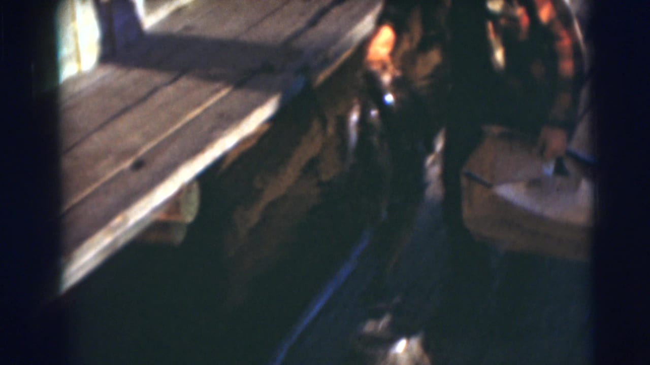 A man in plaid clothing walks alongside the dock in Baraboo, Wisconsin, carrying fishing gear and what appears to be a fish.