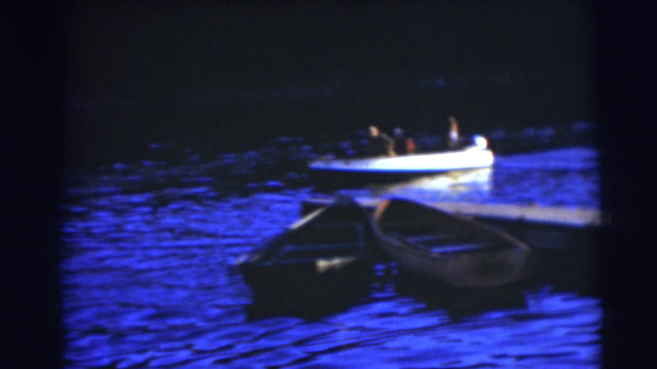 Two rowboats float near blue water as a small motorboat passes behind them.