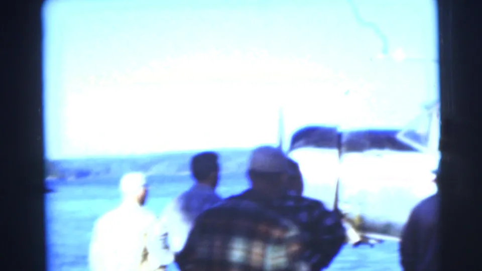 Overexposed 1953 Baraboo, Wisconsin 8mm frame showing people near the lake and a large dark boat or canopy shape above.