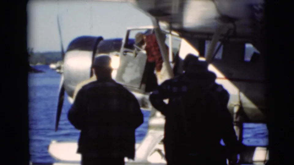 In 1953 Baraboo, Wisconsin footage, several men stand near a seaplane at the lake edge as one figure appears by the door.