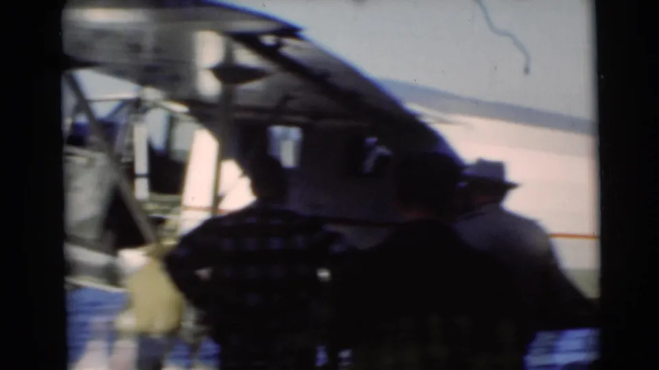 Several men stand in partial shadow beside the seaplane fuselage and wing structure during the Baraboo lakeside home movie scene.