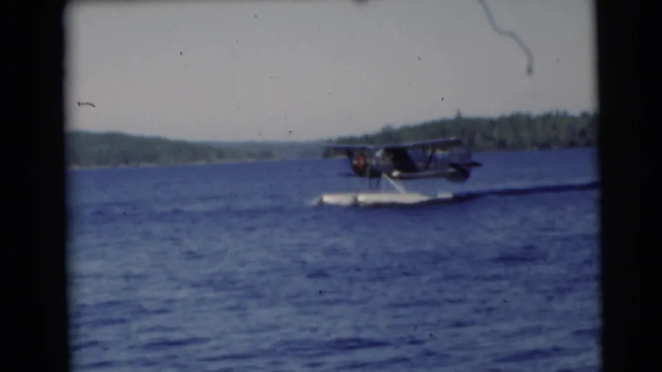 The floatplane continues across the lake in the 1953 Wisconsin home-movie footage, seen against low wooded hills.