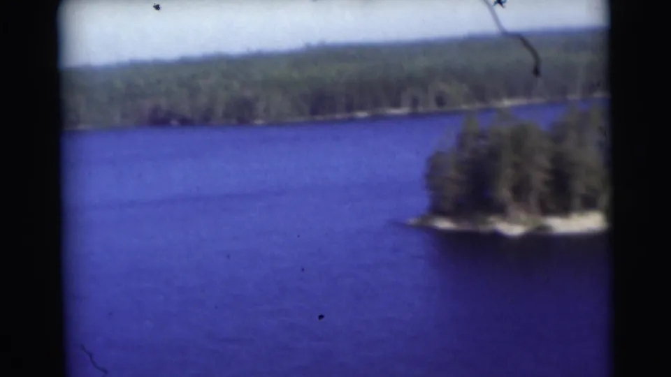1953 Baraboo, Wisconsin 8mm lake frame showing a small wooded island against blue water and a distant forested shore.