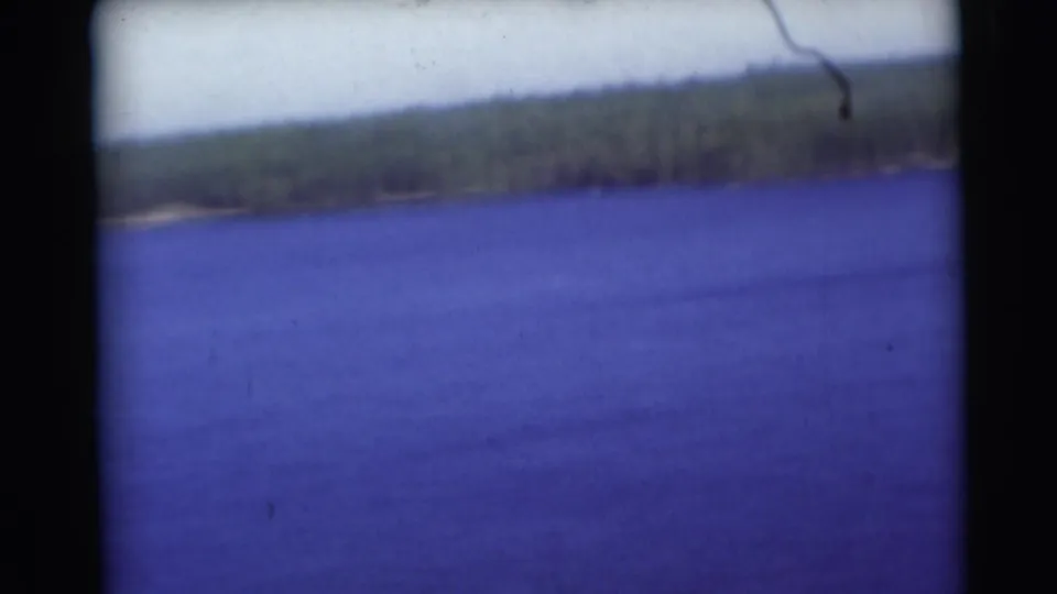 1953 Baraboo, Wisconsin home-movie frame showing blue water, a tree-lined far shore, pale sky, and dark 8mm frame edges.