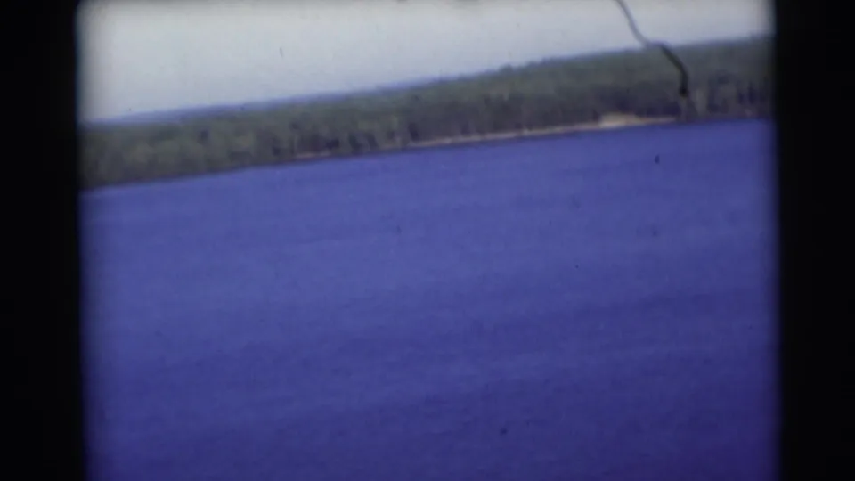 1953 Baraboo, Wisconsin frame with open blue water, a distant treeline, pale sky, and visible 8mm gate edges.